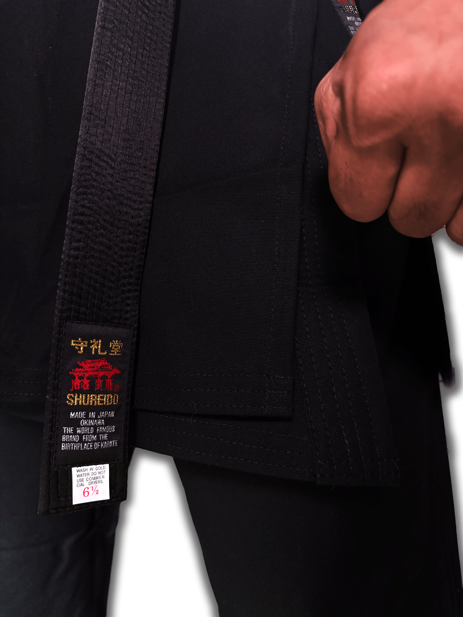Close-up view of the heavy-duty reinforced stitching and premium cotton canvas fabric on the hem of a black Shureido karate gi jacket.