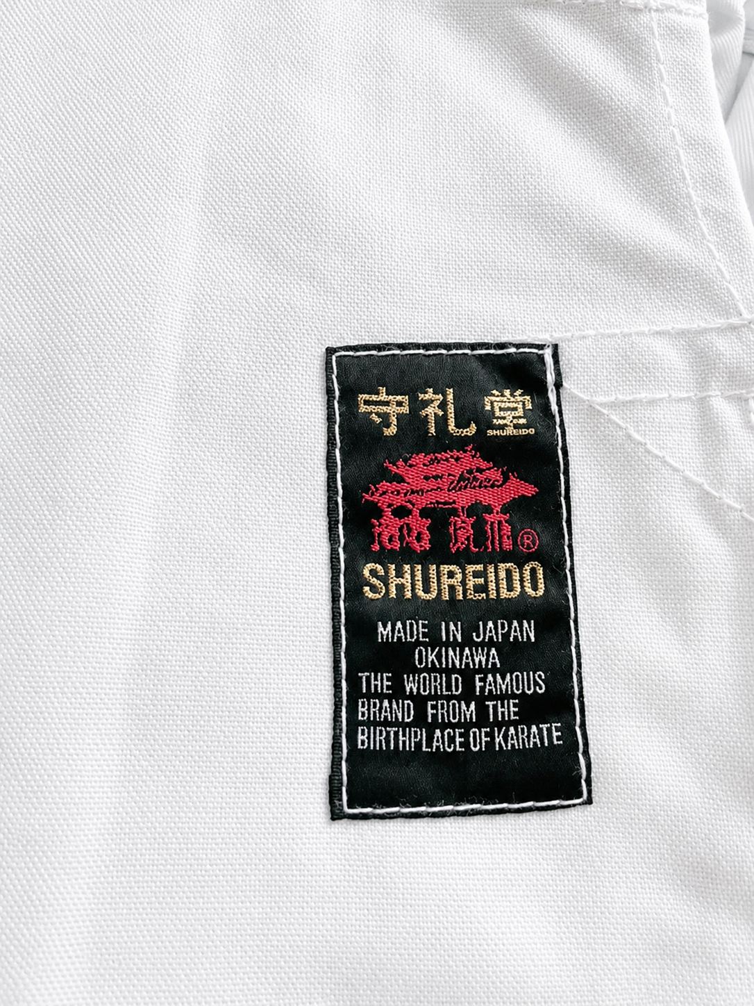 Close-up of the authentic Shureido lapel tag on the Heavyweight K10 Gi, verifying its Made in Okinawa, Japan origins.
