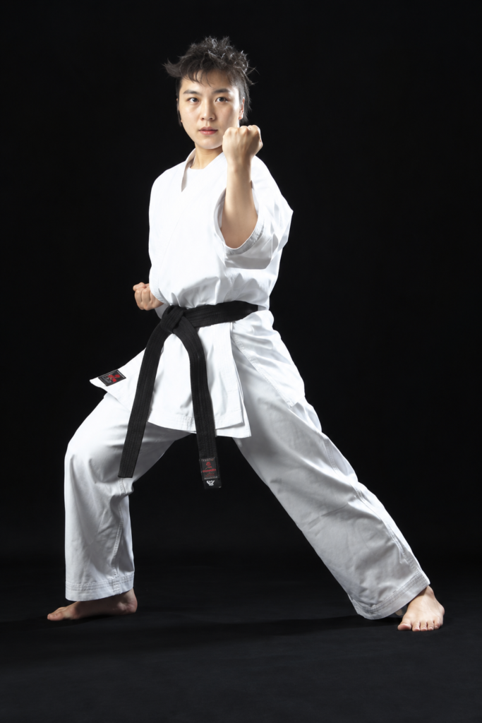 Female black belt martial artist striking a deep front stance, wearing a white Shureido Medium Weight All-Purpose GI
