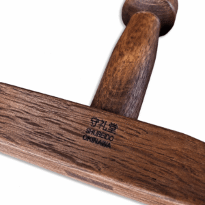 Detailed product photograph of two traditional Shureido Okinawan wooden tonfa resting on a dark textured surface, showing the stamped logos and natural wood grain.