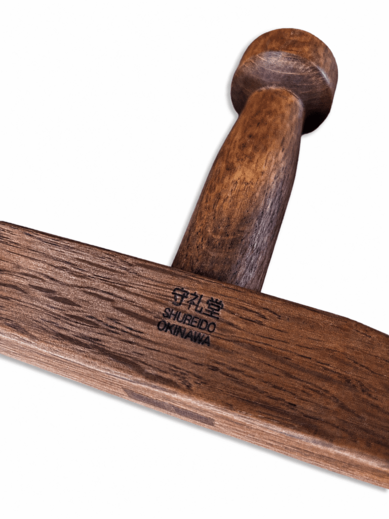 Detailed product photograph of two traditional Shureido Okinawan wooden tonfa resting on a dark textured surface, showing the stamped logos and natural wood grain.