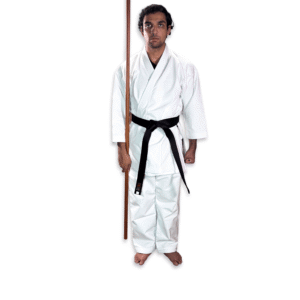 Martial artist in white karate gi and black belt holding a traditional Shureido Okinawan wooden bo staff in a ready stance against a clean background.