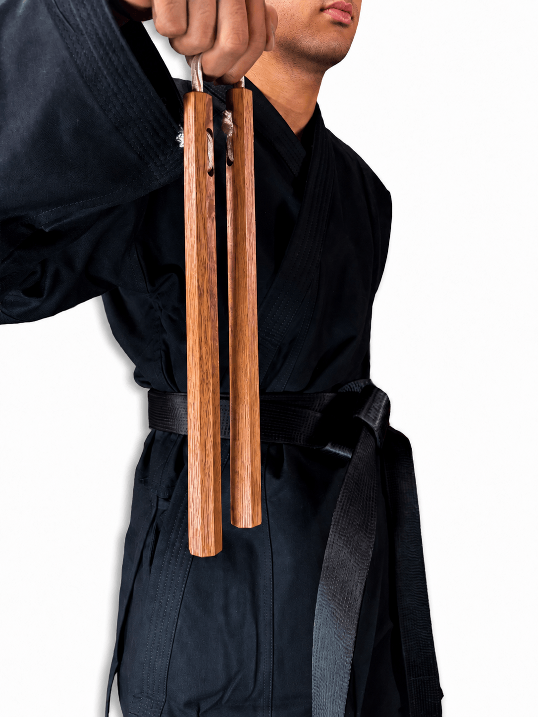 Martial artist in a black karate uniform holding a pair of traditional Shureido wooden nunchaku by the connecting cord against a clean white background.