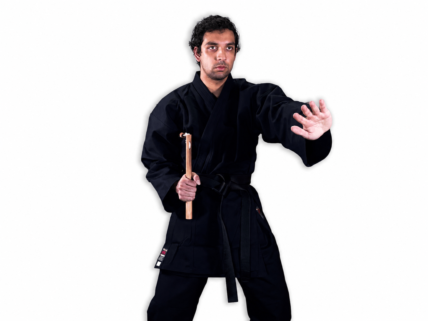 Martial artist wearing a black karate gi demonstrating a ready stance while holding traditional wooden Shureido nunchaku in one hand.