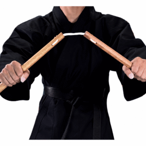Close-up of a martial artist in a black karate gi holding traditional Shureido wooden nunchaku, showing the octagonal handles and connecting cord.