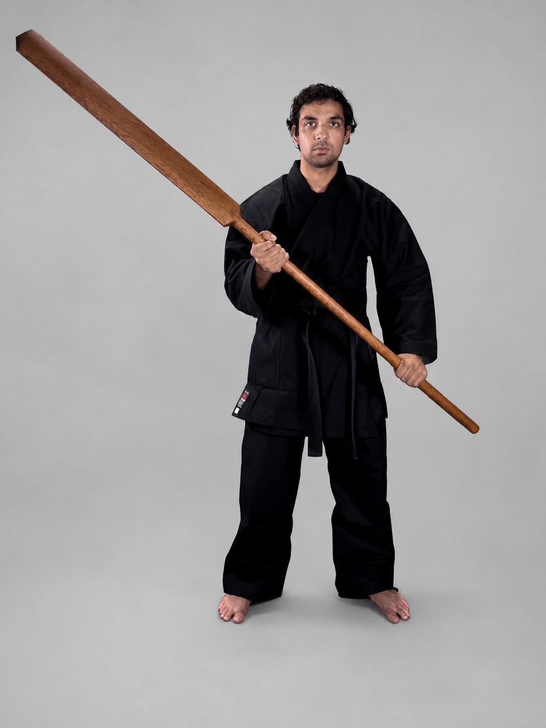 Martial artist wearing a black karate gi and black belt standing upright and holding a traditional Shureido Okinawan wooden eku oar weapon